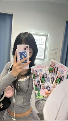 a woman taking a selfie with her cell phone in front of her face and several photos behind her