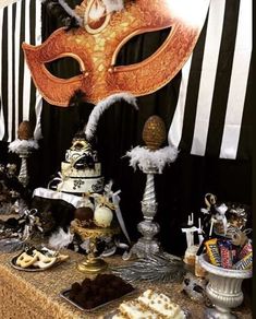 a masquerade mask on top of a table with desserts and candies