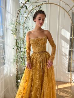 a woman in a yellow gown standing next to a window