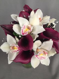 a vase filled with purple and white flowers on top of a gray table next to a wall