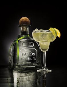 a bottle of patron and a glass with a lemon slice on the rim next to it