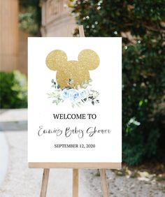 a welcome sign for a baby shower with a gold mickey mouse on it and blue flowers