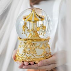 a person holding a snow globe in their hands with gold trimmings and designs on it