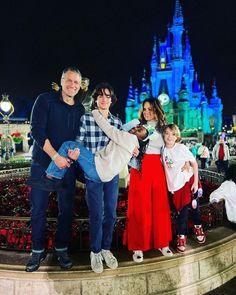 a family poses for a photo in front of the magic kingdom castle at christmas time