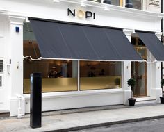 a store front with black awnings on the windows and white buildings in the background