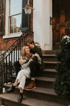 a man and woman sitting on the steps in front of a building with their arms around each other