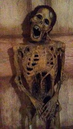 a creepy looking skeleton hanging from the side of a wooden wall with it's mouth open