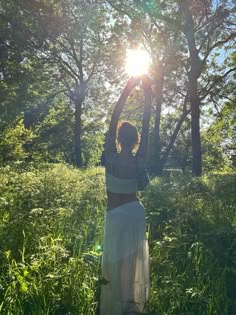 a woman is standing in the grass with her arms up to the sun above her head