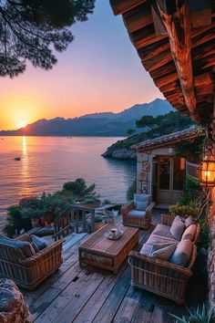 an outdoor deck with wicker furniture and the sun setting over water in the background