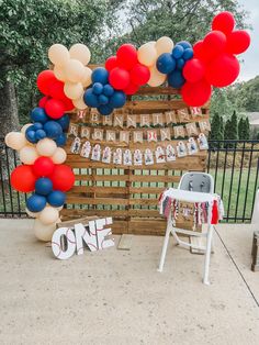 an outdoor birthday party with balloons and decorations on the table, including a sign that says one