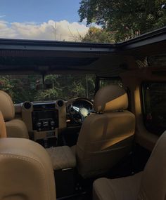 the interior of a vehicle with tan leather seats and dash board, looking out over trees