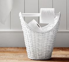 a white wicker basket with two rolls of toilet paper in it on a wooden floor