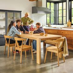 a group of people sitting around a wooden table in a room with lots of windows