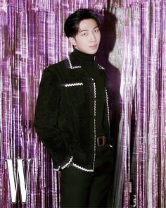 a young man standing in front of a purple curtain wearing a black jacket and pants