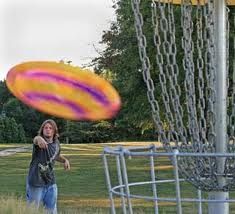 a young man throwing a frisbee into a metal basket on top of a field