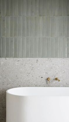 a white bath tub sitting next to a wall with grey tiles on the walls and floor