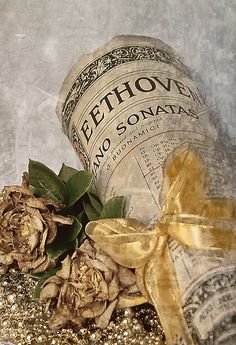 an old fashioned bottle with some flowers on the ground next to it and a bow