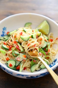 a white bowl filled with noodles and cucumber on top of a wooden table