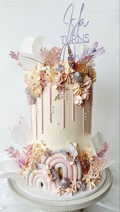 there is a white cake with pink and purple decorations on the top, along with butterflies