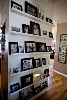 a wall filled with lots of pictures and framed photos next to a wooden floor in a living room