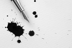 a pen sitting on top of a piece of paper with ink splatters around it