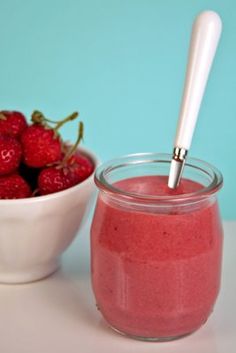 a bowl of strawberries next to a jar of smoothie with a straw in it