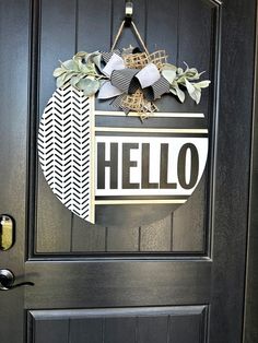 a black door with a hello sign hanging on it's side and some leaves