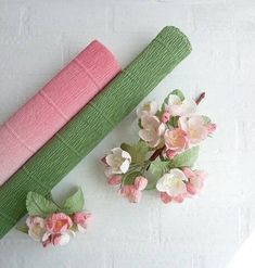 two pink and green napkins next to flowers on a white tablecloth with brick wall in the background