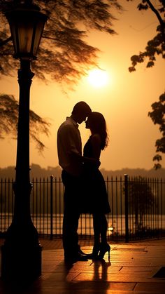 a man and woman kissing in front of a street light at sunset with the sun behind them