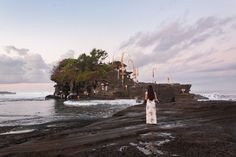 a woman standing on top of a rocky beach next to the ocean with an island in the background