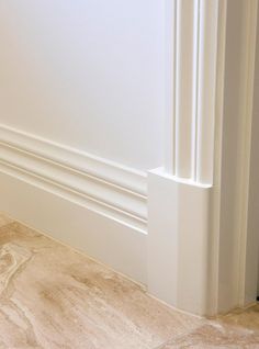 the corner of a room with white walls and marble flooring, along with an open door