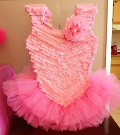 a dress made out of pink tulle sitting on top of a wooden table in front of a wall