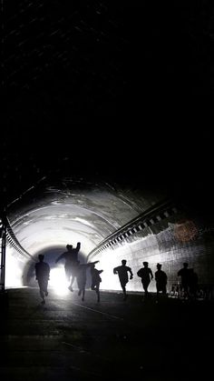 silhouettes of people walking through a tunnel in the dark with light at the end