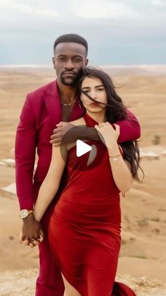 a man in a red suit and woman in a red dress standing on top of a desert