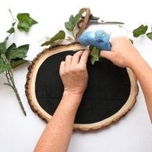 two hands are working on a piece of wood that has been decorated with flowers and leaves