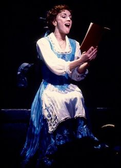 a woman in blue and white dress holding a book while sitting on a chair with her eyes closed