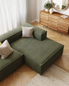 a green couch sitting on top of a hard wood floor next to a dresser and mirror