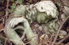 an old statue laying on the ground with its head in it's hands and eyes closed