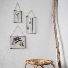 three framed pictures hang on the wall above a wicker stool and small tree branch