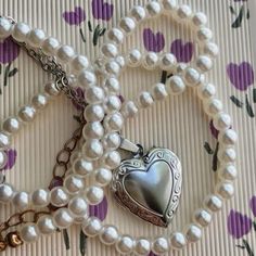 a white necklace with a heart shaped locke on it's chain and pearls around the clasp