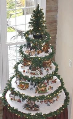 a christmas tree is decorated with miniature train tracks and trees in the shape of houses