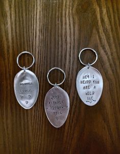 three metal keychains with words on them sitting on a wooden surface, one has a heart and the other has an inscription