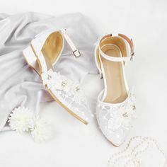 a pair of white shoes sitting on top of a bed next to a necklace and flower