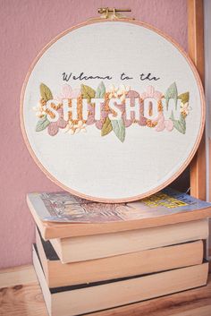 there is a cross stitch pattern on top of some books and a book bag that says, welcome to the shitshow