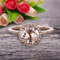 a ring with an oval cut diamond surrounded by small white and pink flowers on a wooden surface