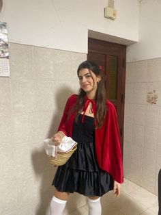 a woman in a red coat and black dress is holding a basket while standing next to a wall