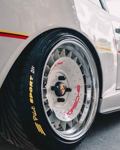 the front wheel of a white sports car with red and yellow lettering on it's rim