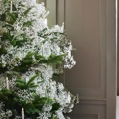 a white christmas tree with candles and flowers in the corner next to an open door