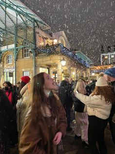 a crowd of people standing around each other in front of a building with snow falling on the ground