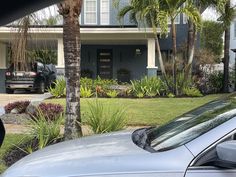 a car parked in front of a house next to palm trees and flowers on the side of the road